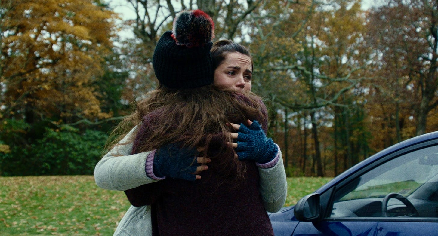 Katherine Langford as Meg Thrombey (left) and Ana de Armas as Marta Cabrera (right) in KNIVES OUT. The two are hugging.