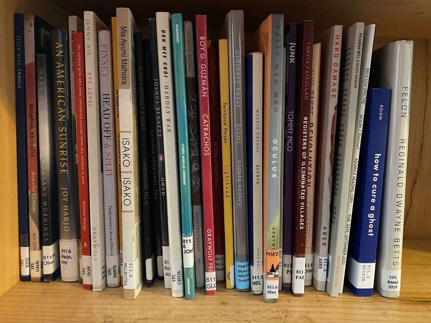 A shelf of ~30 skinny and colorful contemporary poetry collections.