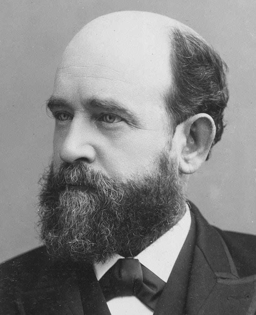A black and white picture of a balding, bearded white man.