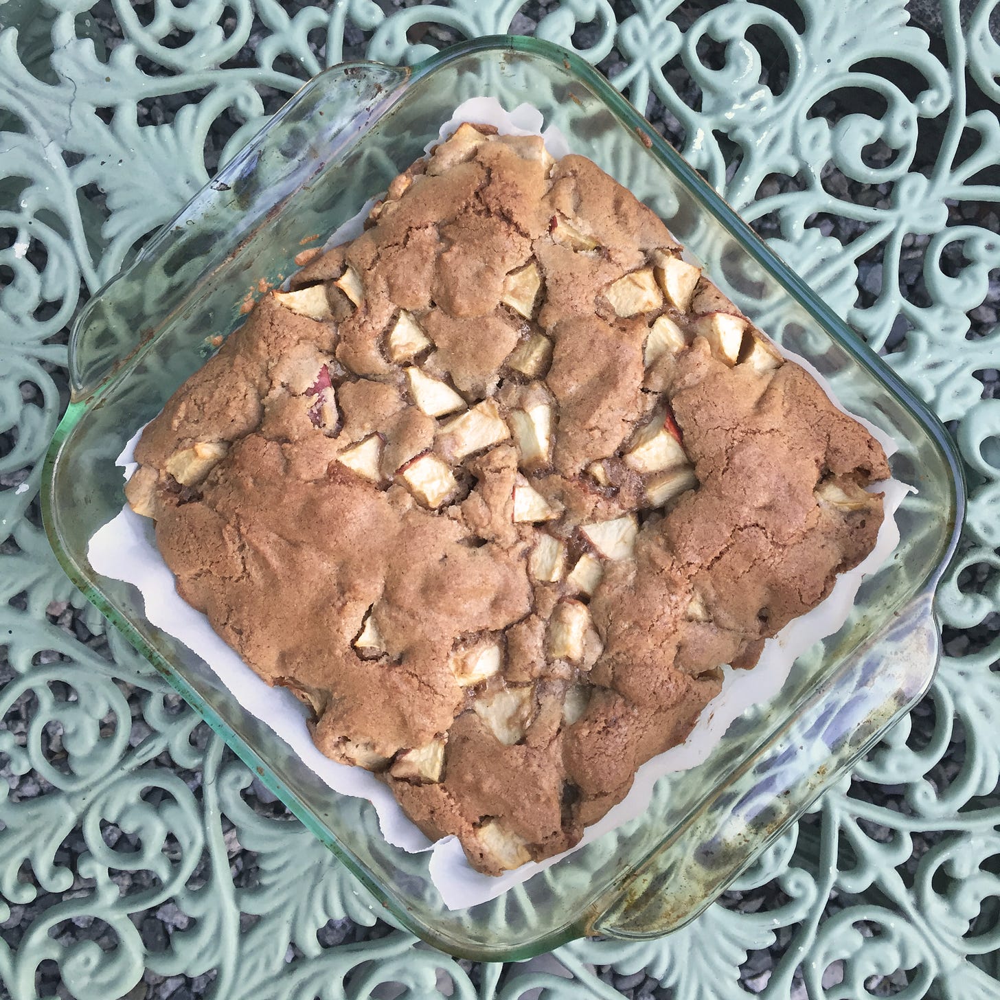 from above, a square glass dish with a browned cake, which has a cracked top and pieces of apple visible throughout.