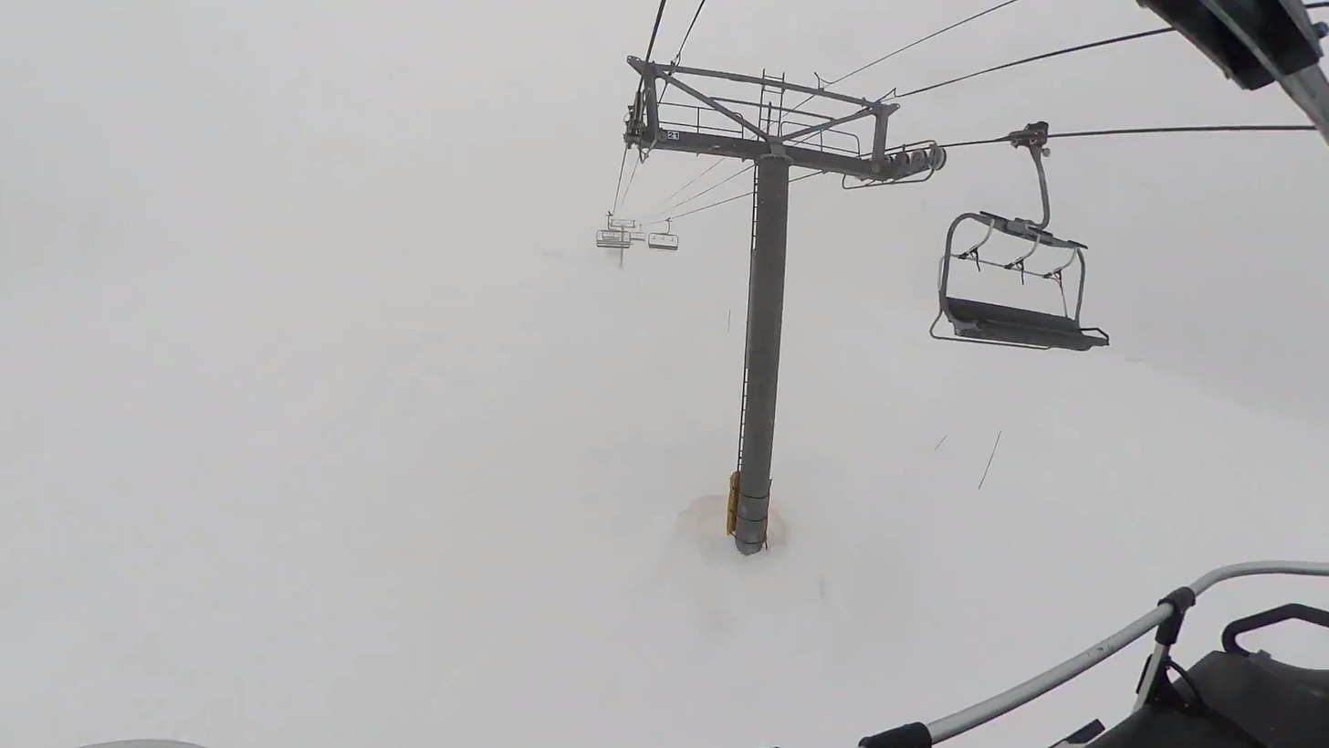 Riding a ski lift in white-out conditions. The sky and ground are indistinguishable. All you can see are the poles, cables, and chairs of the lift.