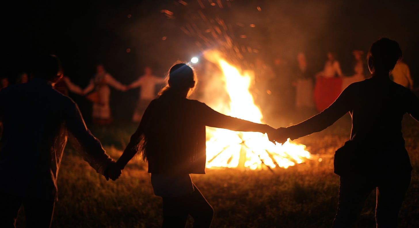 Figures dancing in silhouette around a bonfire 