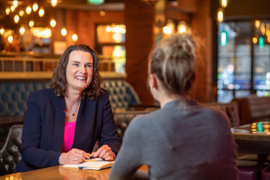 Photo of Lucinda smiling, sitting opposite a woman