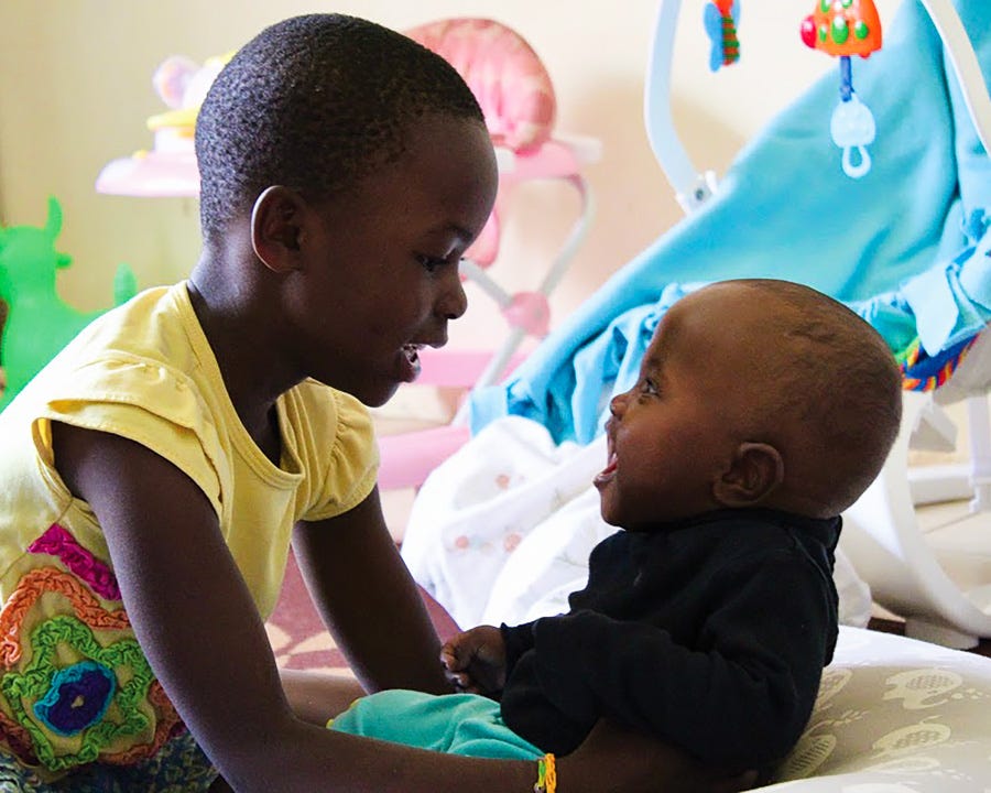 An older sibling plays with a baby in a nursery, Family Keys International, Kenya.