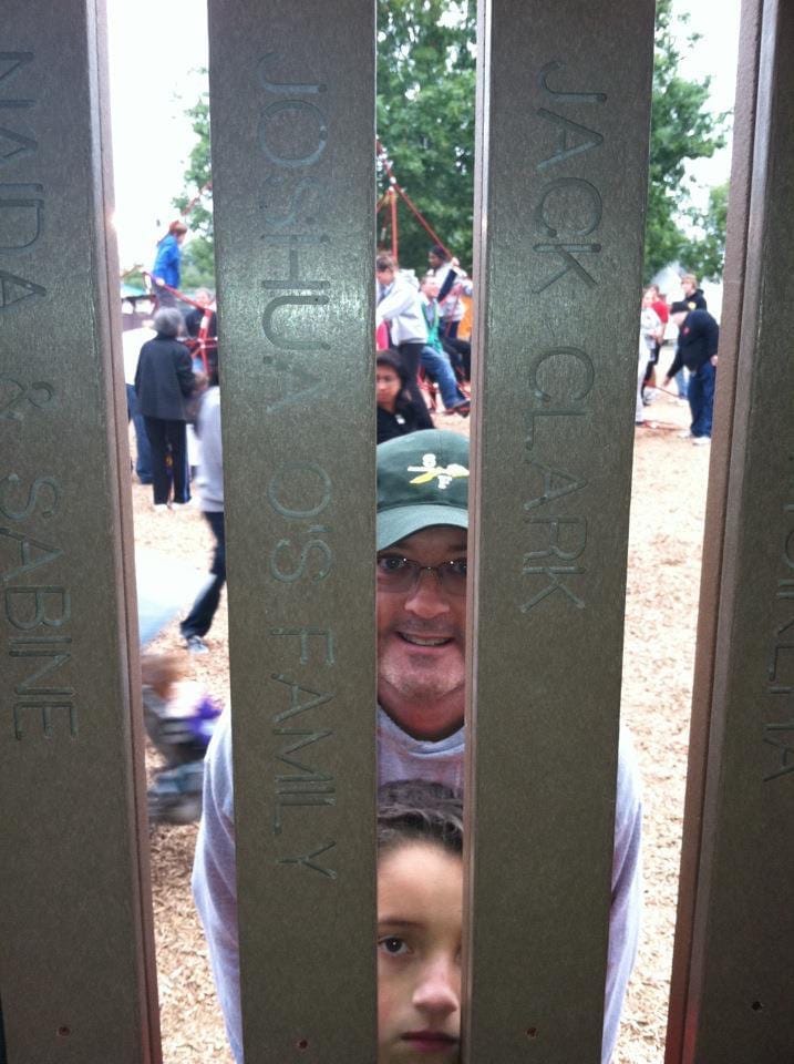 A man and his son peer through posts at a park