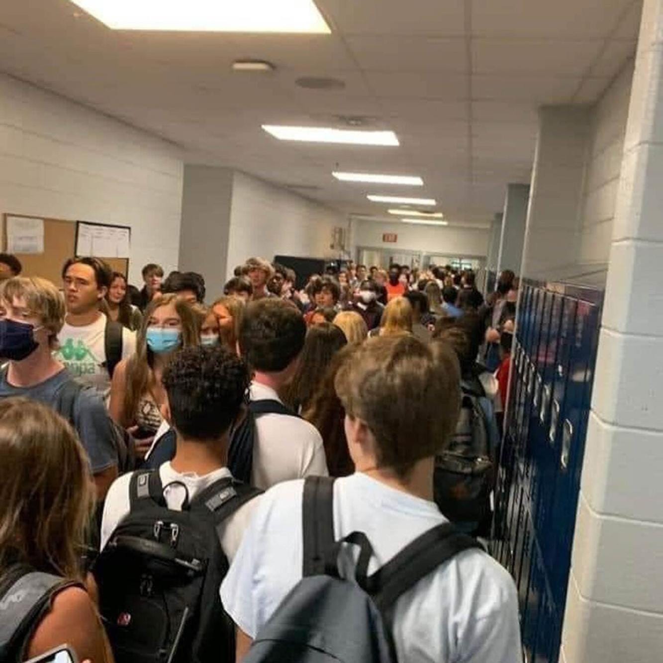 A crowded school hallway. Some students are masked and some are not.