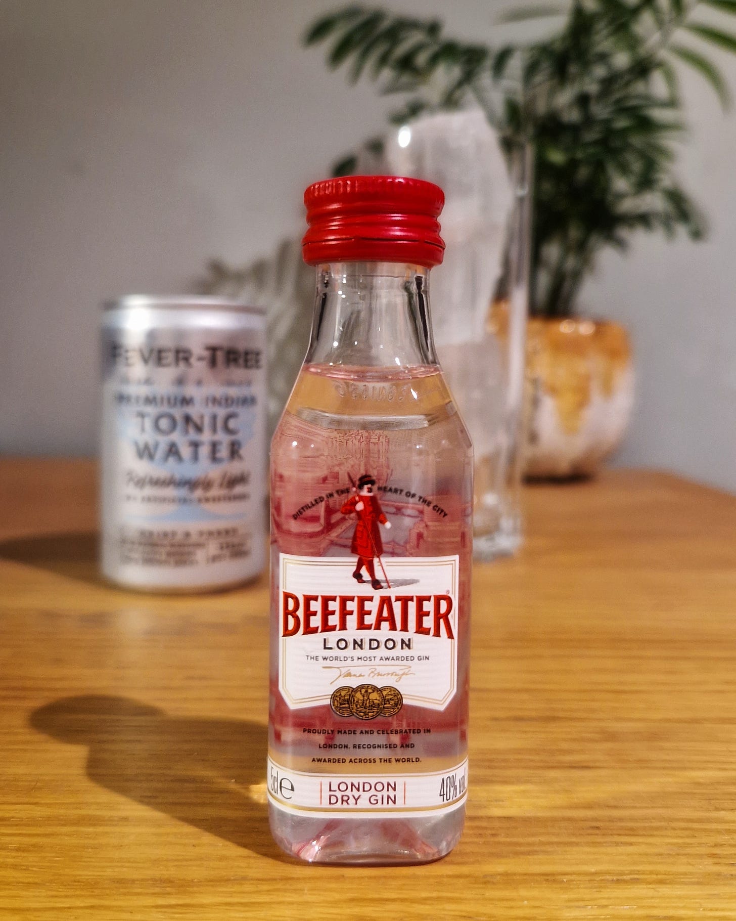 A miniature bottle of Beefeater gin. In the background there is a tin of tonic water and a glass with ice.