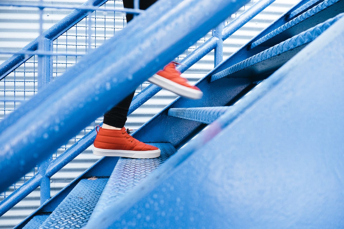 Red sneakers walking swiftly up a blue-tinged metallic staircase.