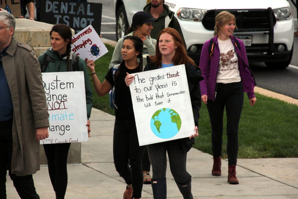 A teenage girl holds a sign that says, "The greatest threat to our planet is the belief that someone else will save it."