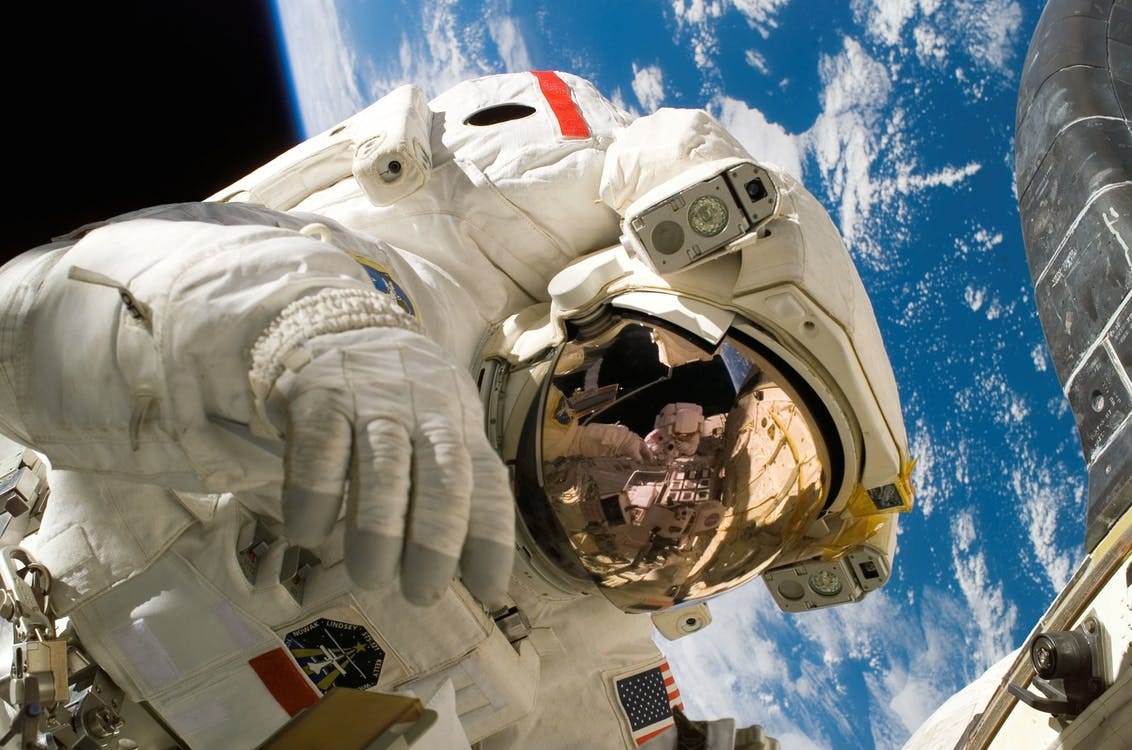 Free This picture shows an american astronaut in his space and extravehicular activity suite working outside of a spacecraft. In the background parts of a space shuttle are visible. In the far background of the picture planet earth with it's blue color and white clouds is shown as well as a patch of black space. Stock Photo