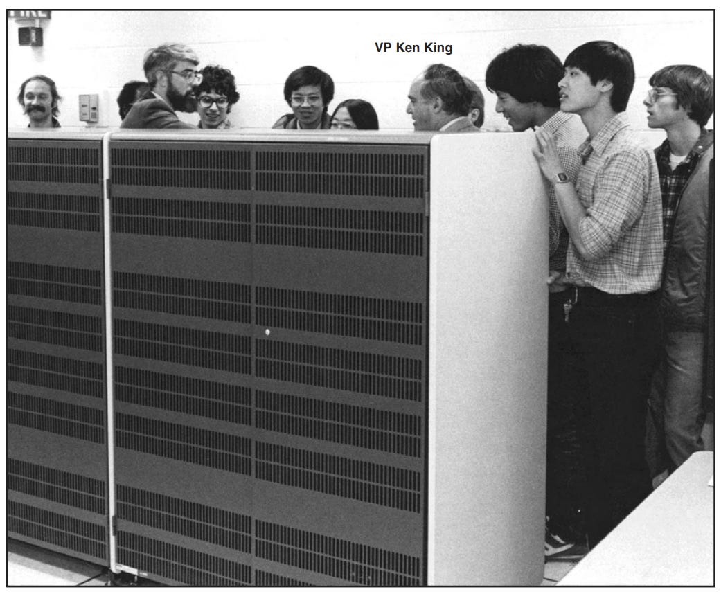 Several people gathered around a mainframe computer that is very large--like two refrigerators.
