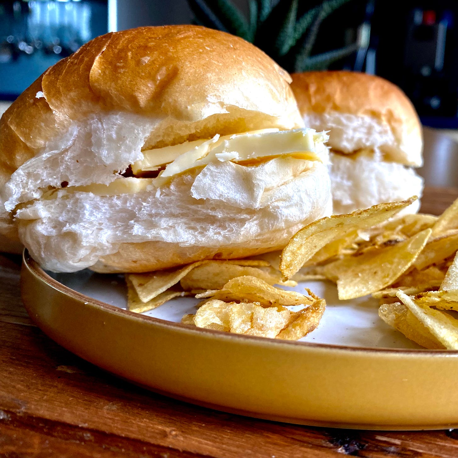 Yellow plate with two soft white bread rolls filled with cheese, a few crisps to the side.
