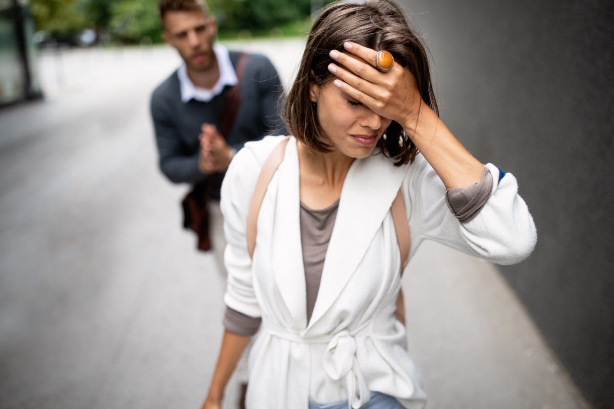 A woman walks away from her partner with a sad look on her face and her head in her hand.