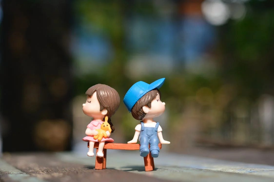 Image of figurines sitting on a bench with a blurred out background from Pexels Pengwhan.