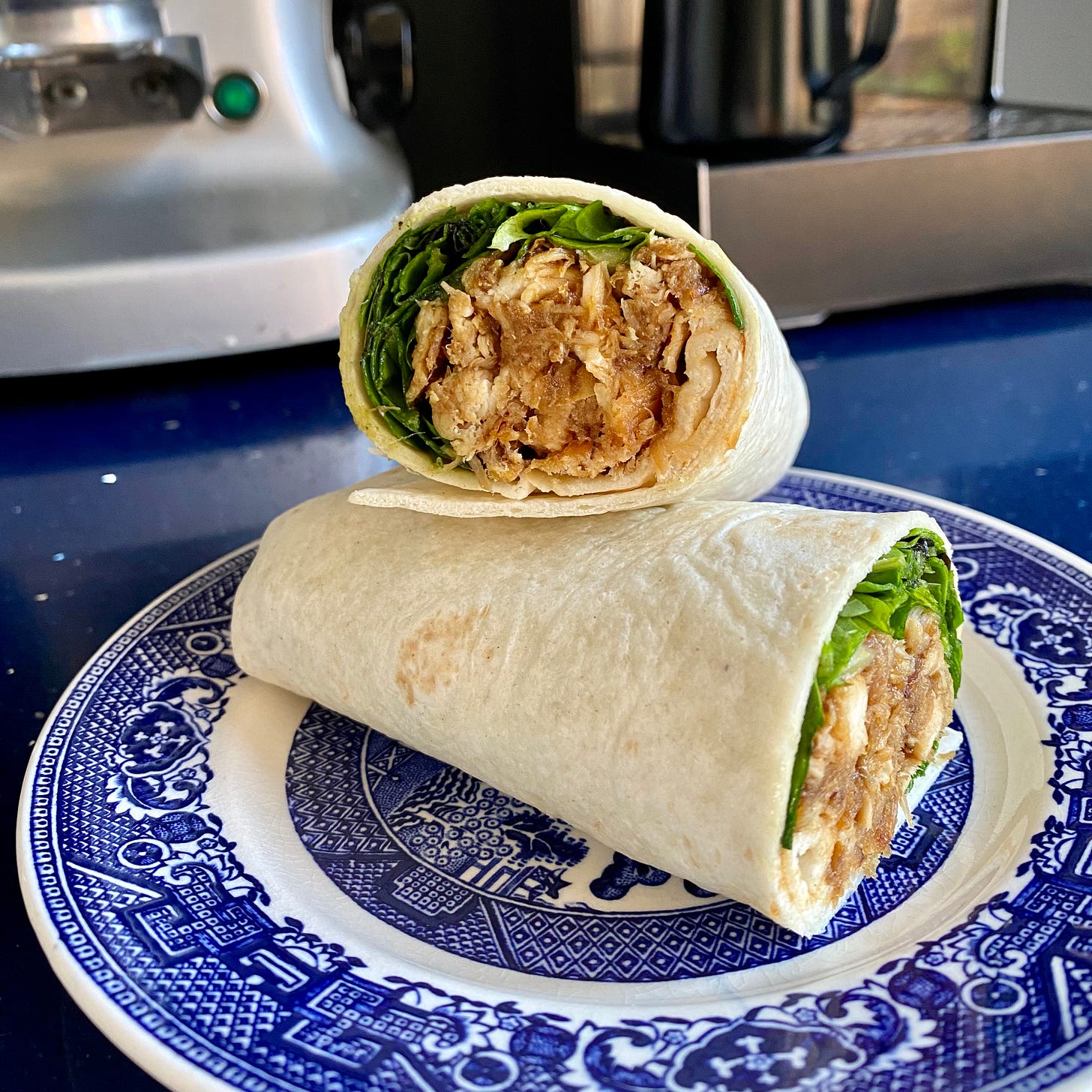 Blue and white plate with a cut-open sandwich wrap filled with shredded chicken and salad