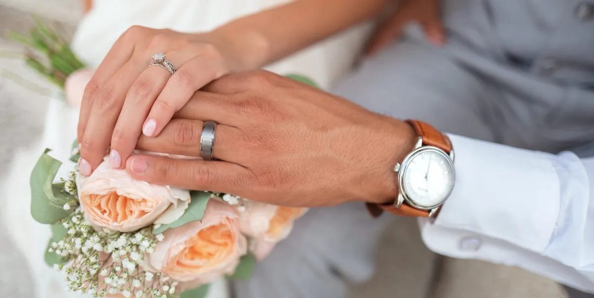Two hands with rings placed over a bouquet of flowers