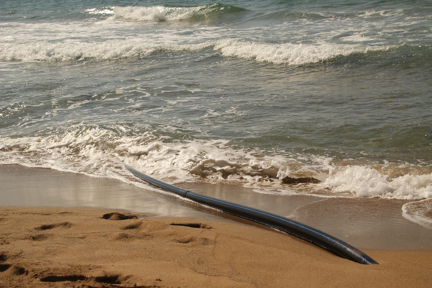 A black cable on a beach disappears into the ocean surf.