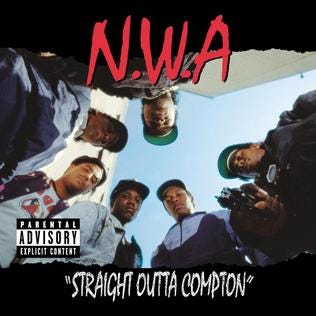 The members of N.W.A. look down to the camera and Eazy-E points a gun to it