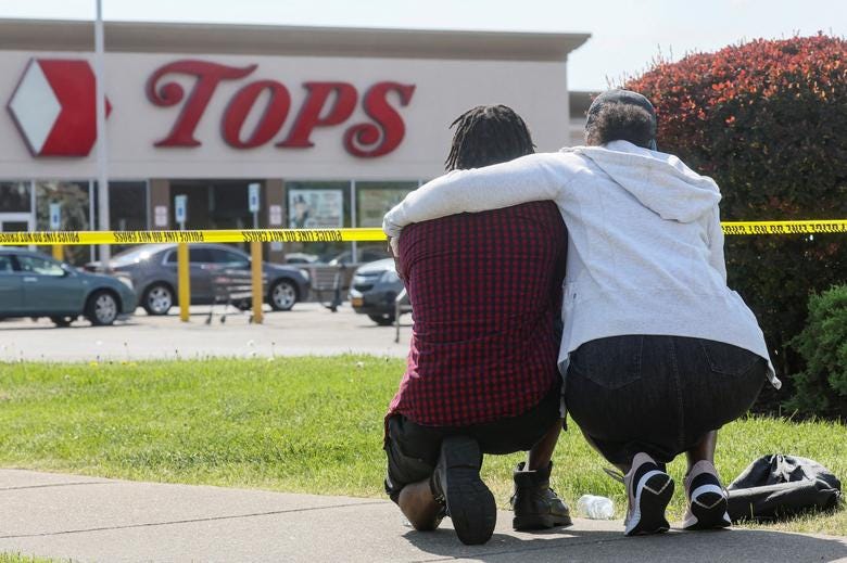 Two Black mourners crouching in front of Tops grocery story in Buffalo, NY