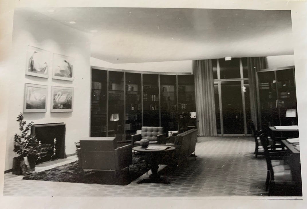 Black and white photo of the Sterling Morton Library, showing a couch and armchairs in front of a fireplace and surrounded by an oval of bookshelves.