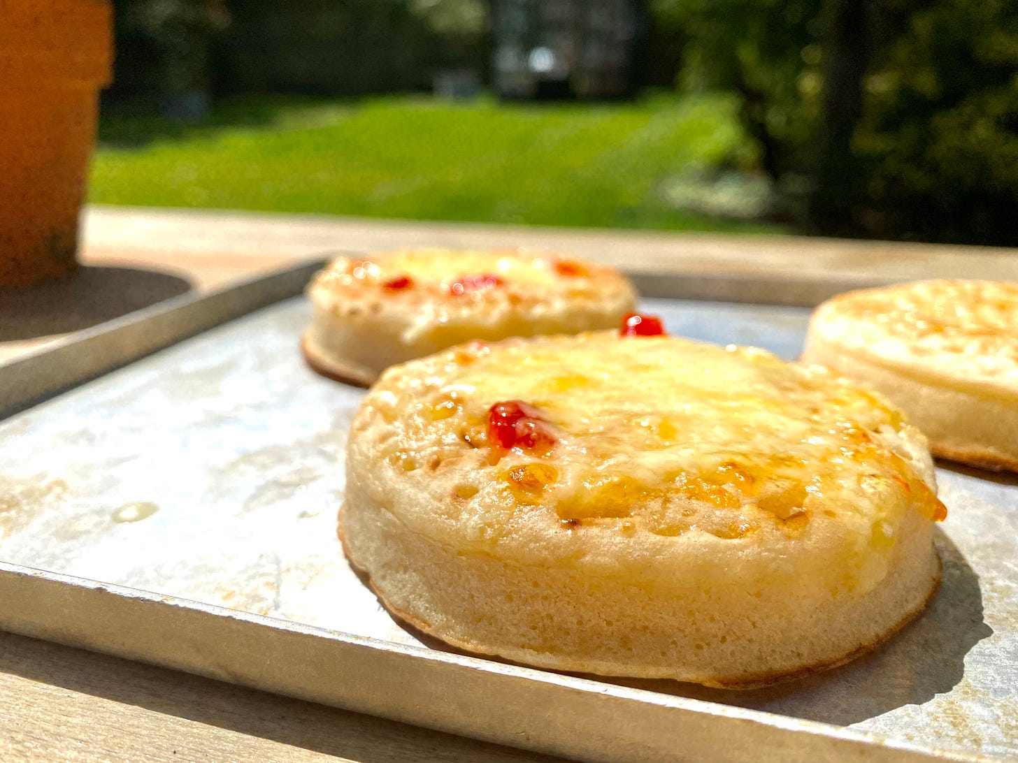 Cheese topped crumpets with flecks of chilli jam on a metal oven tray, in the garde.