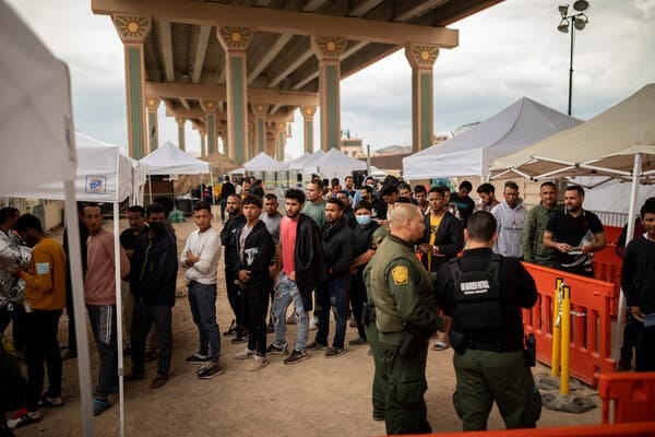 A group of migrants standing under a bridge with U.S. Customs and Border Protection officers.