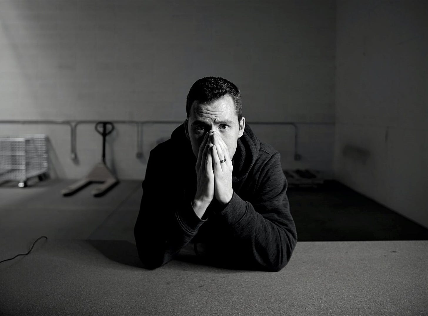 black and white photo of man sitting in empty warehouse with hands covering his mouth