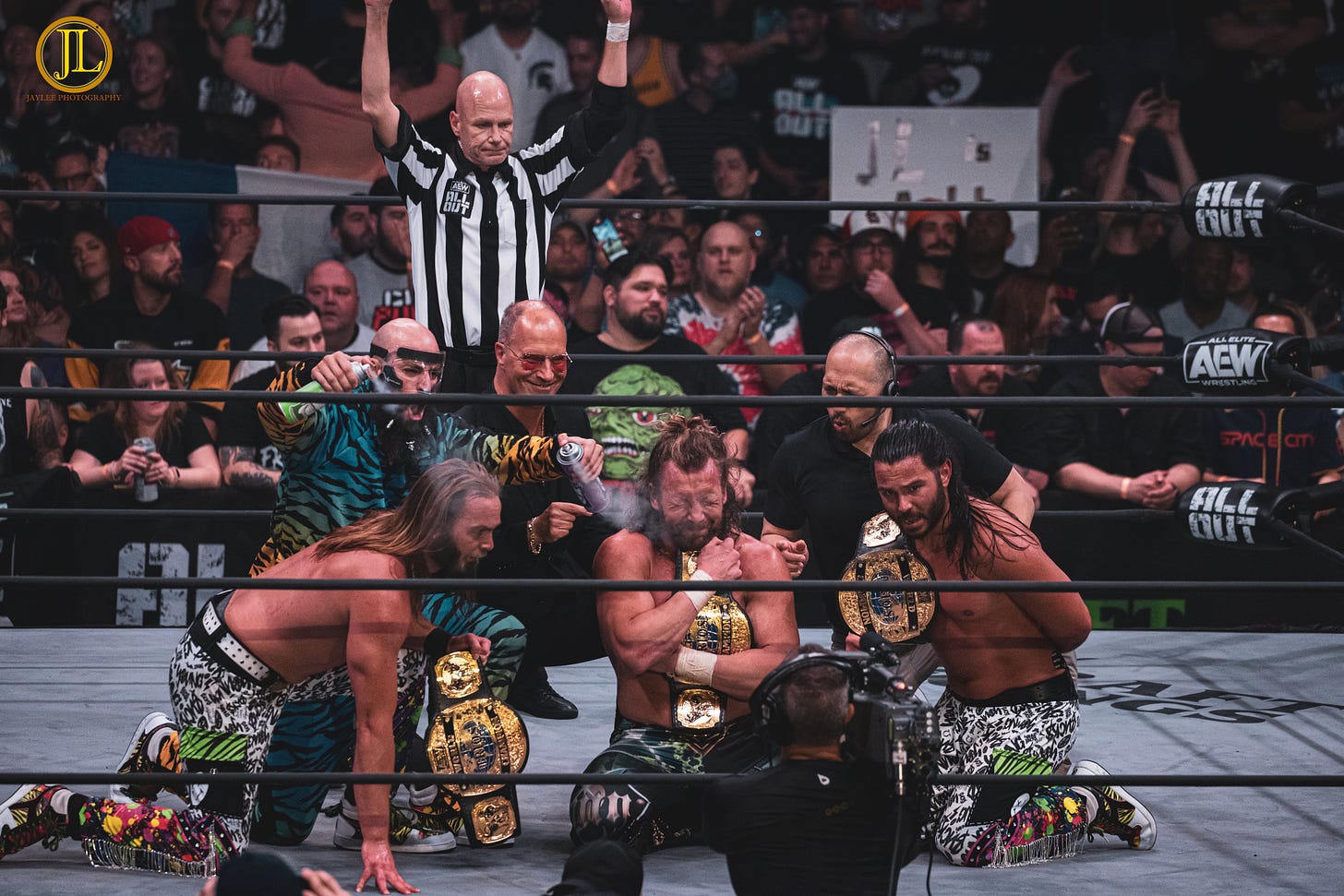 The Elite celebrates with the trios title belts at All Out, with Kenny Omega getting Brandon Cutler's freeze spray in his eyes