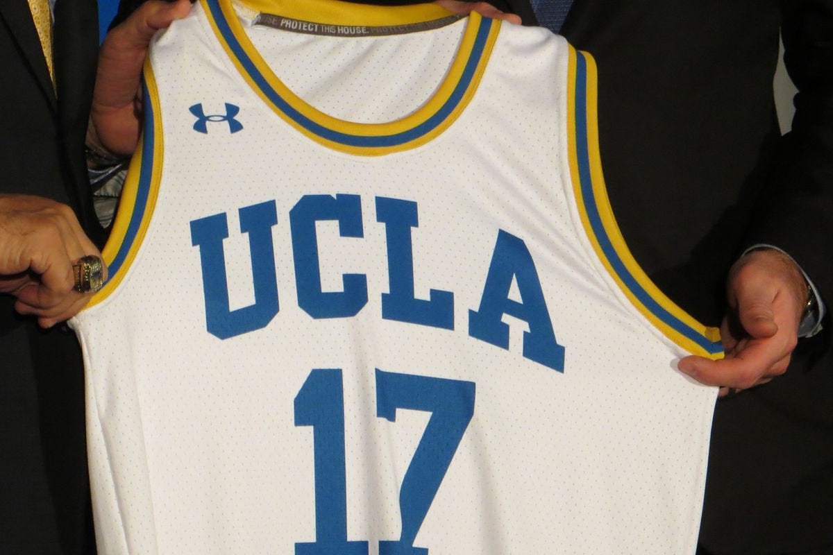 UCLA AD Dan Guerrero and Under Armour Founder and CEO Kevin Plank hold up a symbolic UA-branded UCLA basketball jersey with the number 17 representing the start of UCLA's contract with Under Armour.