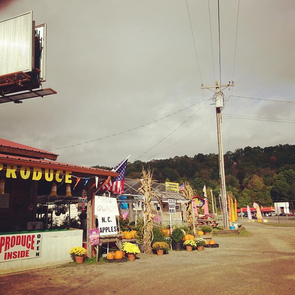 A farmstand in North Carolina in the foothills of the Smokies. It's autum, there's pots of chrysanthemums, squashes and an American flag. It's a little ramshackle. 