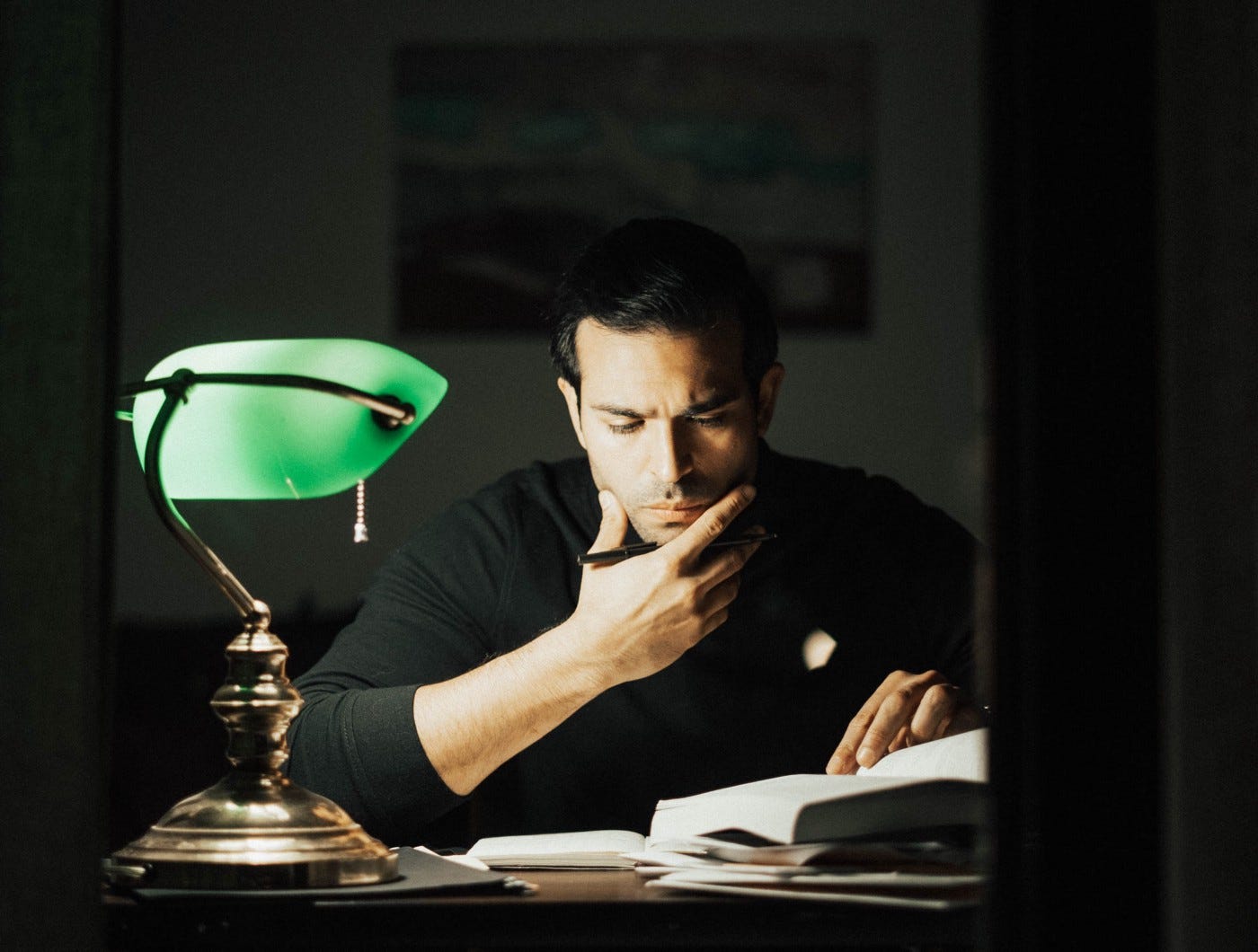 Thoughtful man in a black turtleneck studying by a night lamp