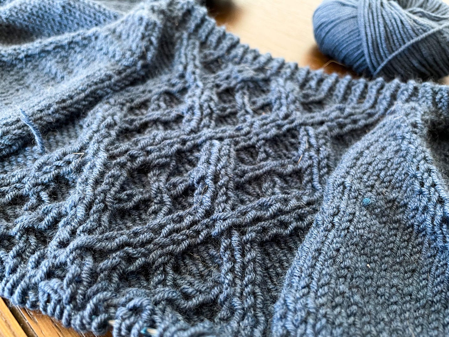 A closeup of a central cable panel on a sweater in progress.