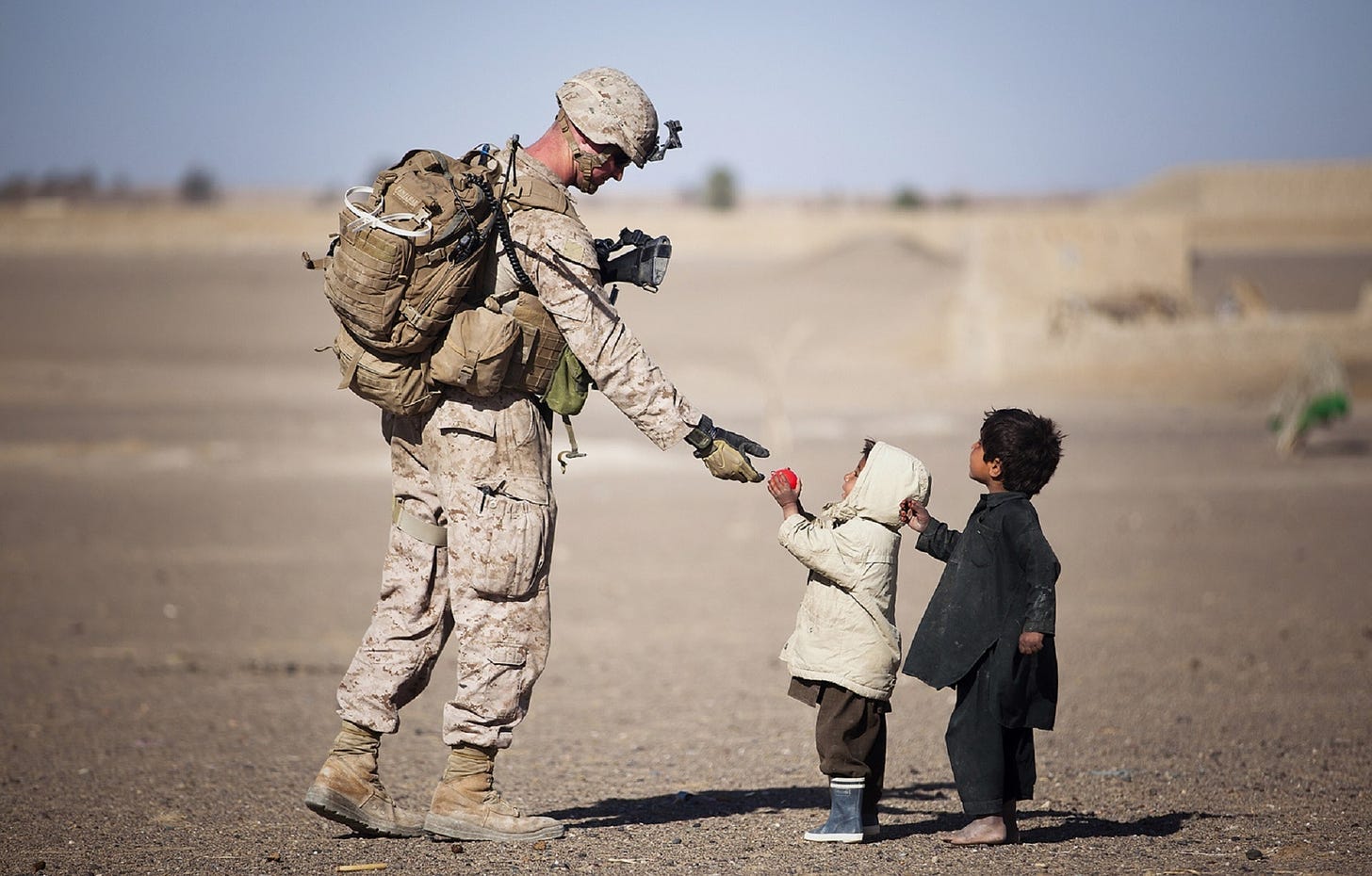 A soldier giving a red fruit to small children during the daytime.