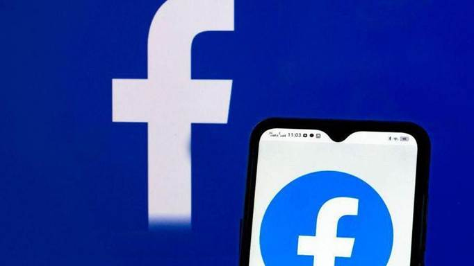 The facebook logo displayed on a smartphone screen, in front of a backdrop of the Facebook logo.