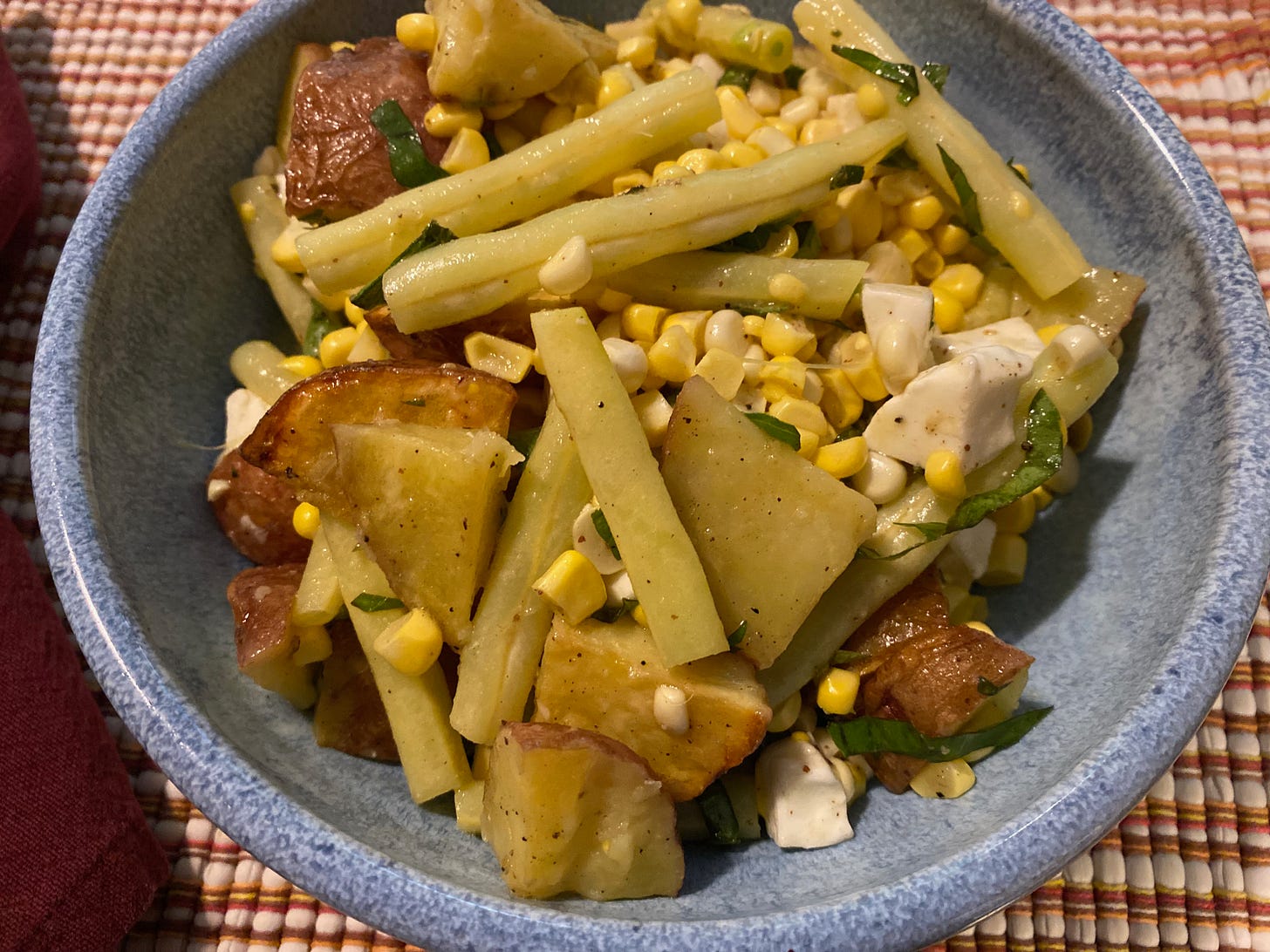 A blue ceramic bowl full of roasted potatoes, yellow wax beans, fresh corn, and chunks of mozzarella. 