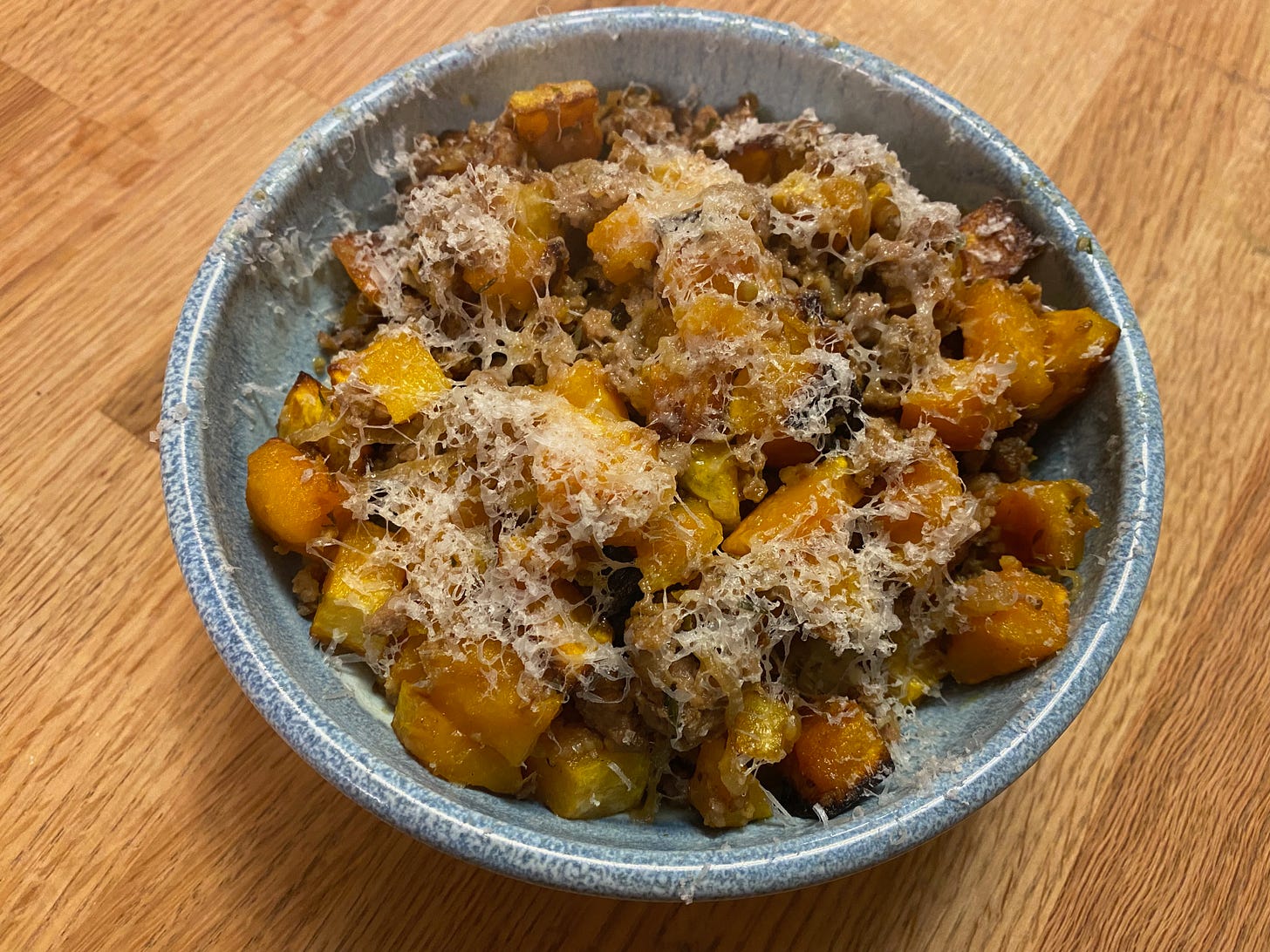 A blue ceramic bowl full of cubbed roasted butternut squash and ground pork covered in grated Parmesan.