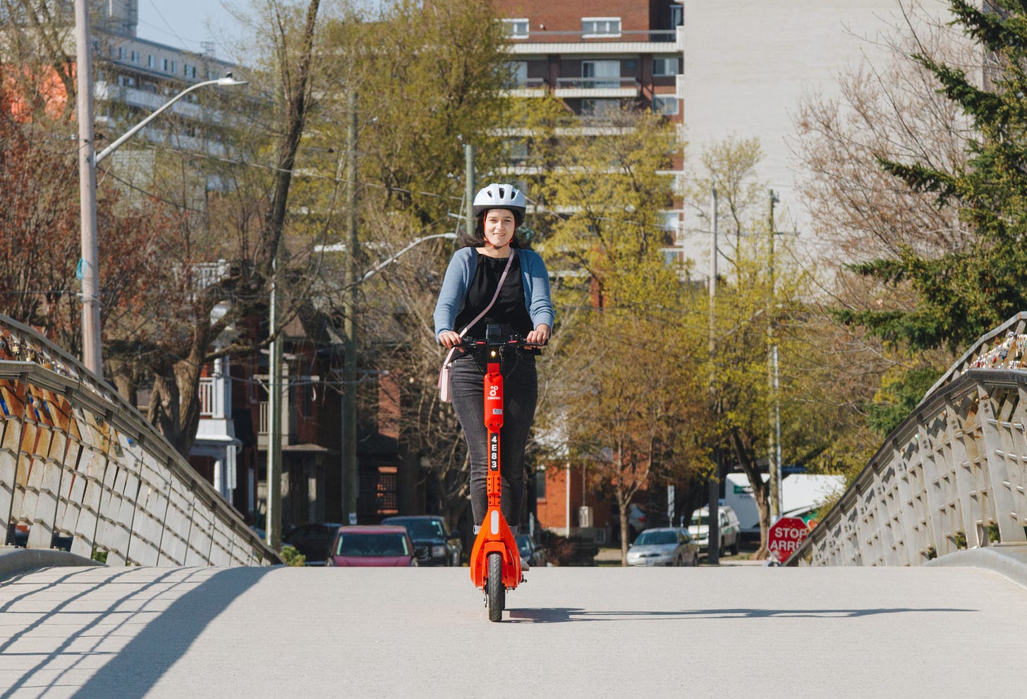 A woman wearing a helmet rides an e-scooter over a footbridge in Ottawa.