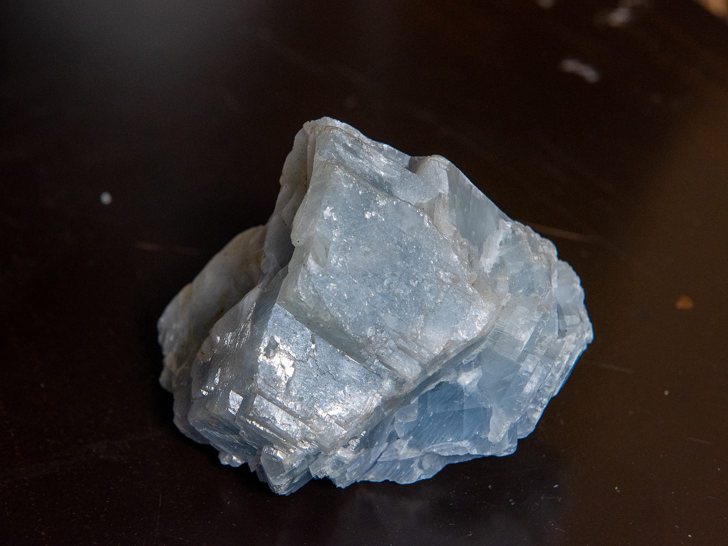 A jagged blue crystal about 4 inches wide on a dark metal surface