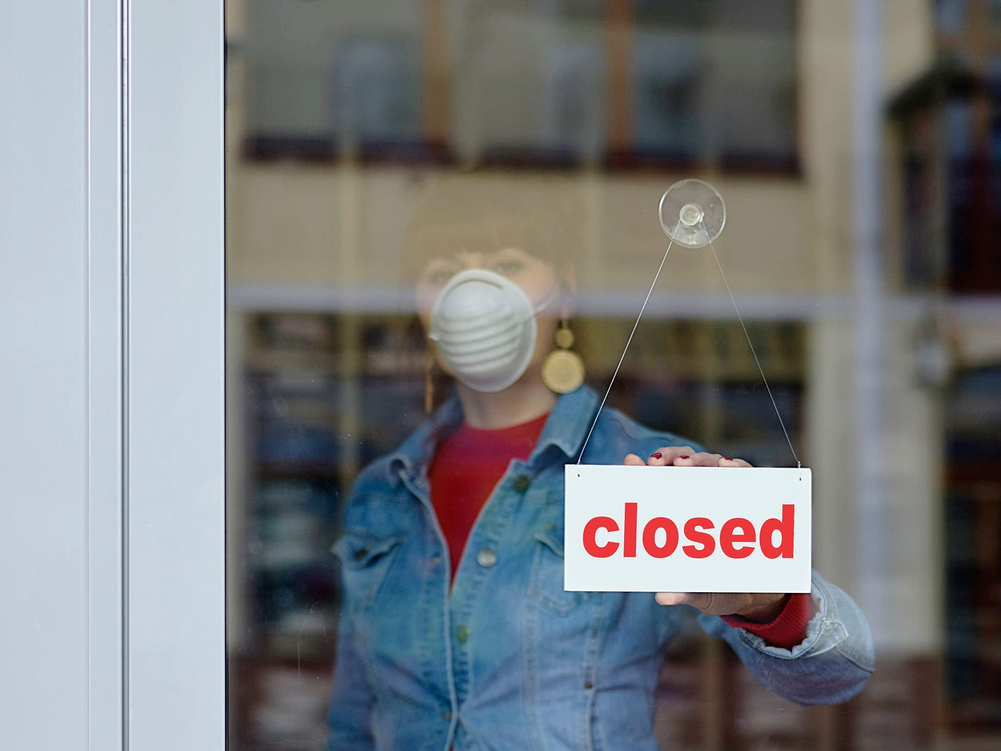 Seorang wanita pemilik toko menutup toko sambil mengenakan masker.