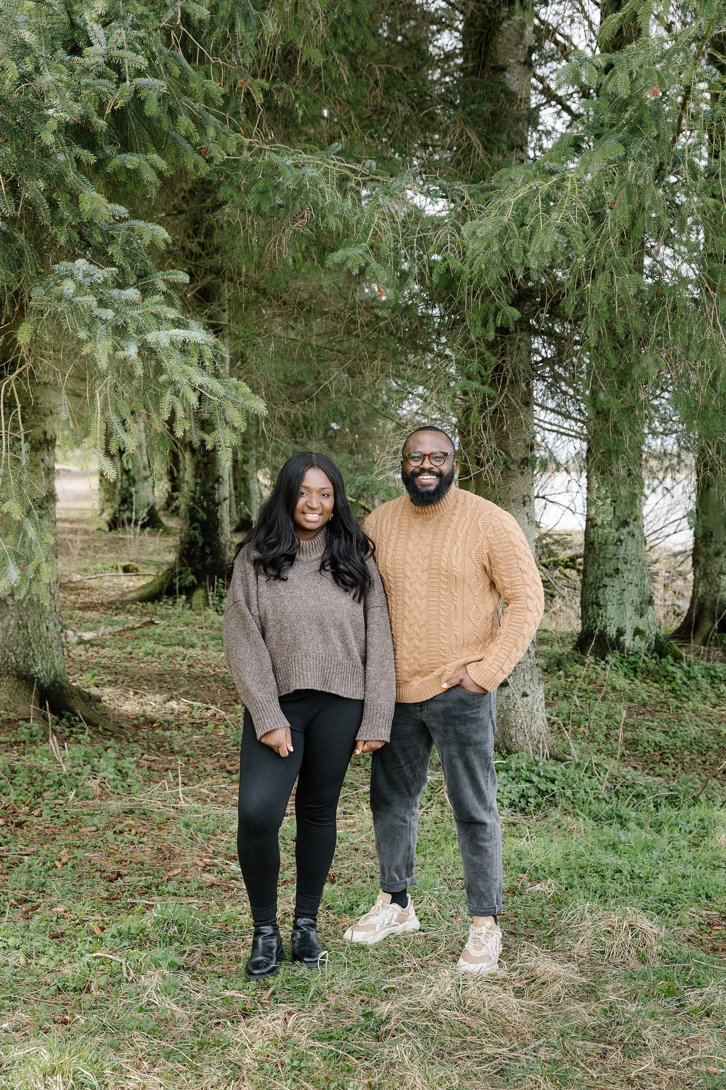 Ebi and Emmanuel of Our Lovely Goods stood smiling in front of some pine woods, they are dressed for autumn.