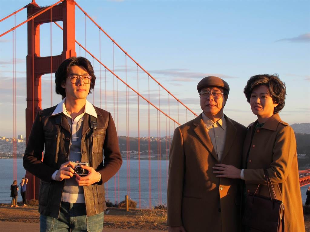 A young man with wavy 1980s hair, and an elderly couple stand in the light of the sunset against the backdrop of the Golden Gate Bridge. A young man with wavy 1980s hair, and an elderly couple stand in the light of the sunset against the backdrop of the Golden Gate Bridge.
