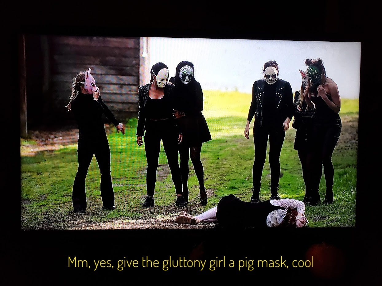 The six masked and black-clad Sins standing over Aubrey on the ground, captioned "mm, yes, give the gluttony girl a pig mask, cool"