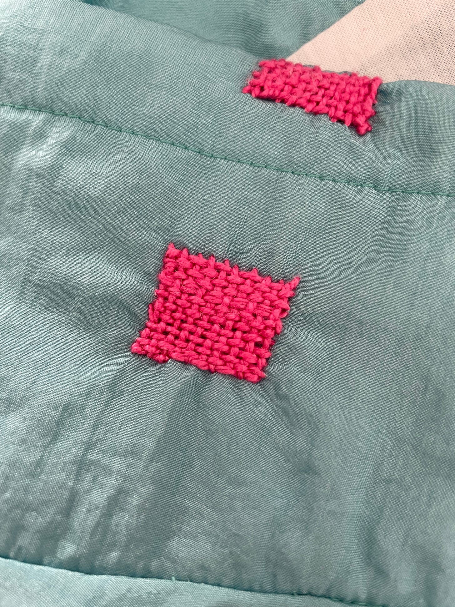 A closeup photo of visible mending on the windbreaker - Katharine has patched the holes by weaving bright pink thread on top.