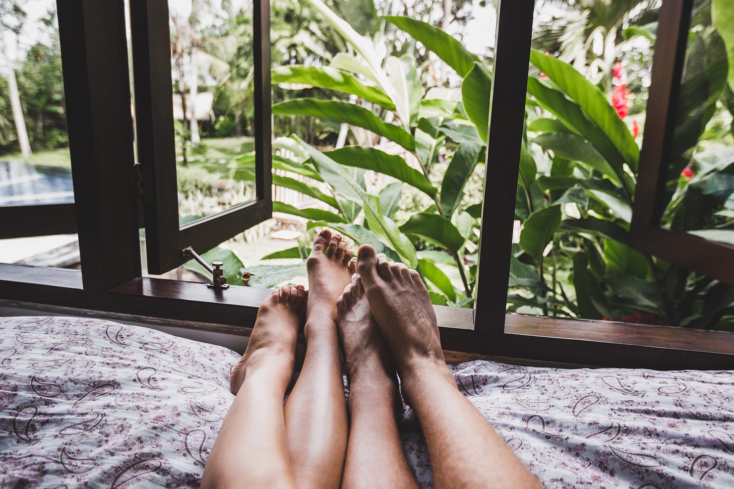 A couple in lies in bed with their legs on the edge of a window looking into the garden.