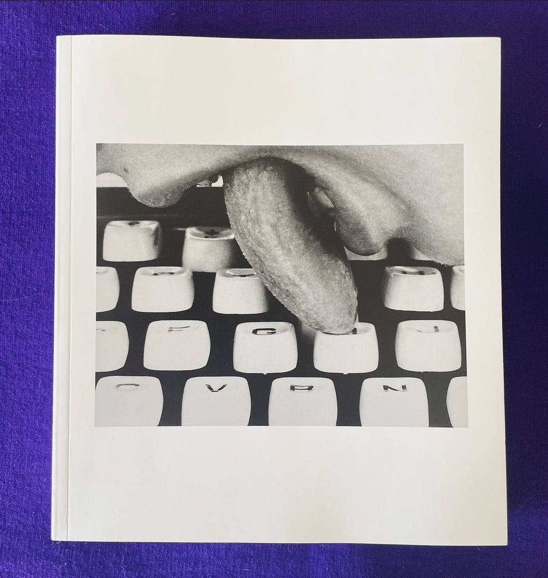 A square white book with a close-up photograph of a woman's mouth and her tongue gently touching the "h" key of a typewriter.