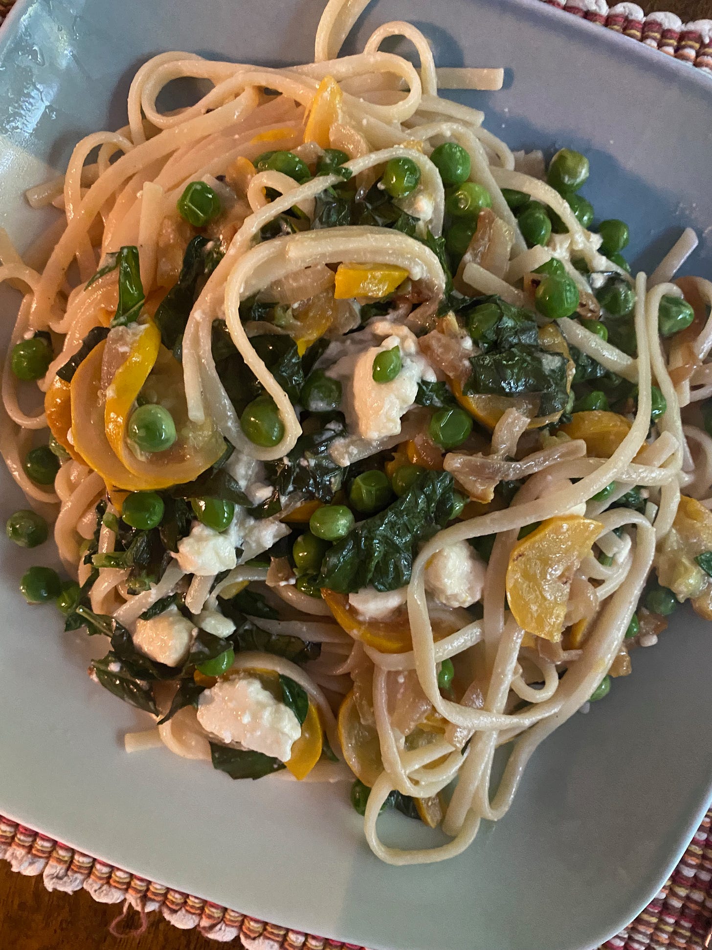 A square plate of linguine mixed with sliced summer squash, peas, chunks of feta, and chopped spinach.
