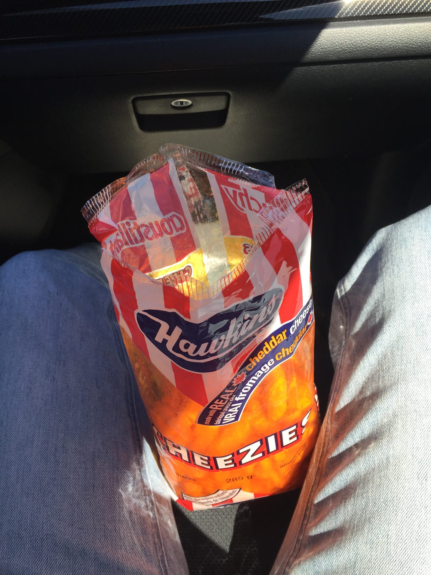 On my lap in the car, a red and white large bag of Hawkins cheezies, open at the top.