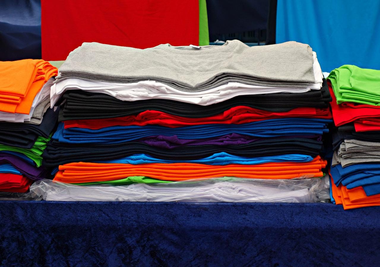 Three stacks of neatly folded tee shirts sit on a table with a blue cover.