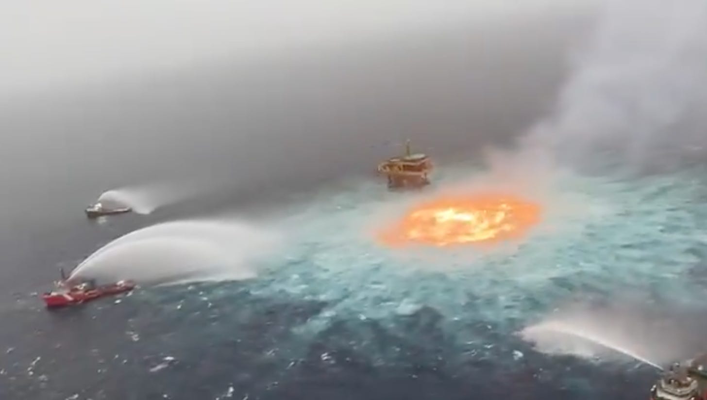 Several boats spray water in the ocean around an orange circle of fire.