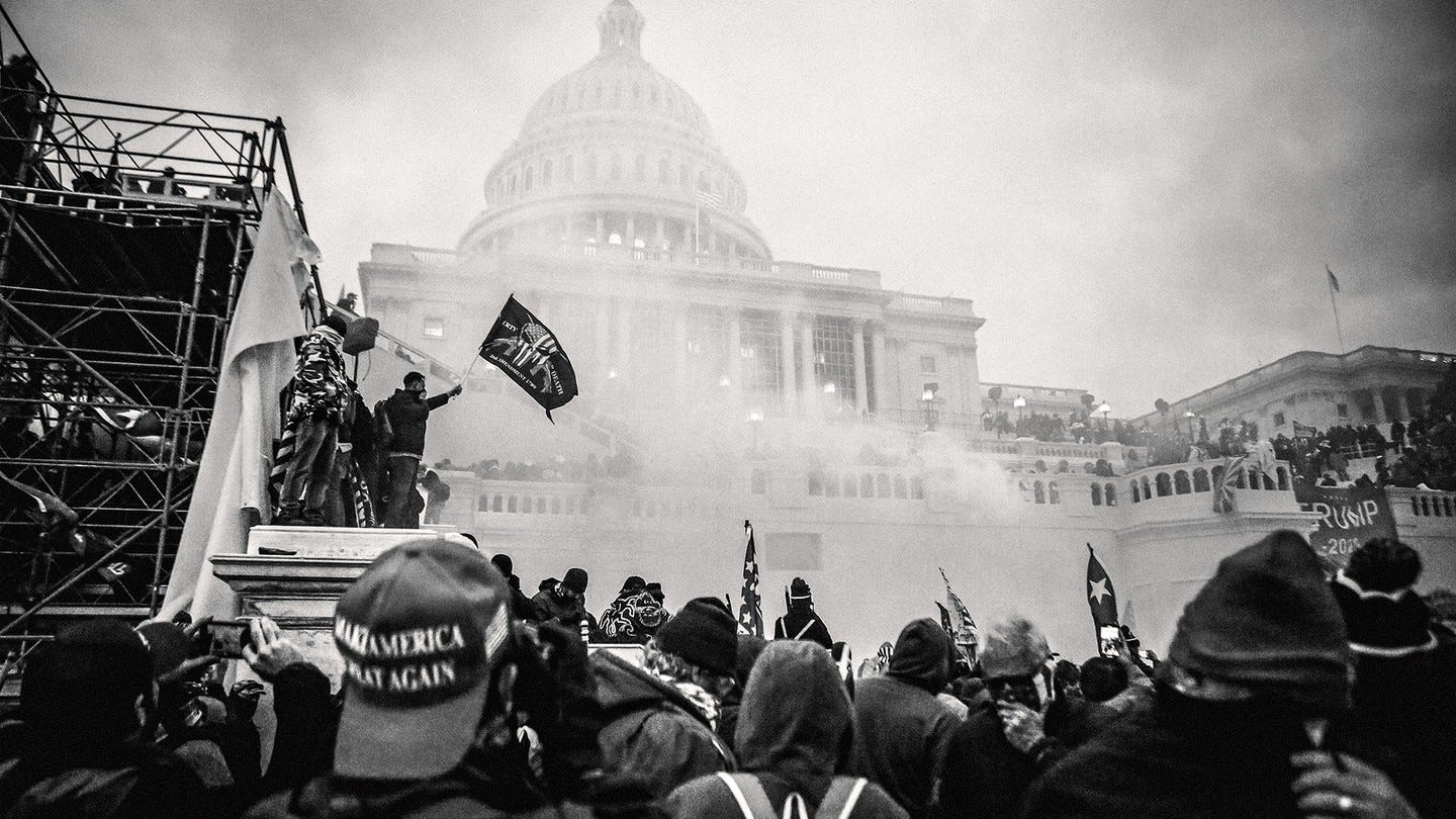Una foto di una folla con un cappello MAGA in primo piano e persone in piedi su un'impalcatura con una bandiera del Secondo Emendamento e uno striscione Trump davanti al Campidoglio degli Stati Uniti oscurato dal fumo